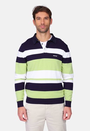 Homme portant un maillot de rugby à manches longues avec des rayures horizontales bleu marine, blanche et vert clair, associé à un pantalon beige clair.