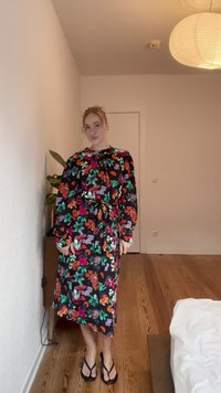 Vestido de manga longa, floral, com fundo preto, apresentando flores coloridas em tons de rosa, verde e laranja, atado na cintura.