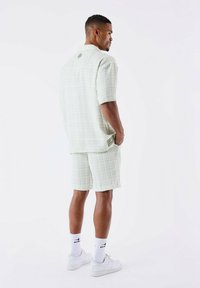 Lichtgroene textuur met korte mouwen shirt en short set, met een boxy pasvorm, subtiel ruitpatroon en labeldetail op de achterkant.
