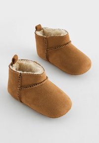 Bottines en suede marron avec une doublure en fourrure douce, présentant des détails de coutures et une petite boucle sur chaque talon pour un enfilage facile.