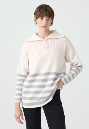Pull à rayures blanches et grises avec col, présente un panneau avant côtelé et deux boutons. Coupe ample avec manches longues et ourlet arrondi.