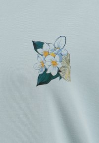 Un tessuto blu chiaro presenta un design ricamato di fiori bianchi con centri gialli e foglie verdi, accompagnato da un'accenno giallo.