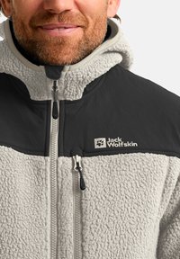 Giacca in fleece con corpo testurizzato grigio chiaro e parte superiore nera e liscia. Presenta una chiusura frontale con zip e un logo sul lato sinistro del petto.