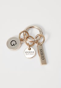 Portachiavi con più anelli; presenta un'etichetta circolare argentata con la lettera "G", un'etichetta rotonda con "GUESS EST.1981" e un'etichetta rettangolare stampata con "GUESS."