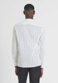 Witte langesleeve shirt gemaakt van lichtgewicht stof met verticale uitsnijding strepen, een standaard kraag en knoopmanchetten, gezien van achteren.