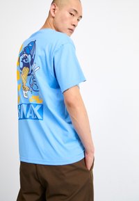 Light blue cotton t-shirt with a graphic print on the back featuring a cartoon character, yellow accents, and "NIKE AIR SNAX" text.