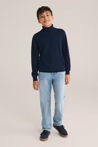 Mornarska pulover turtleneck, dolgi rokavi, rebrasti manšeti in spodnji del; svetlo modri ravni kavbojski hlači; črni športni copati z rjavimi podplati.