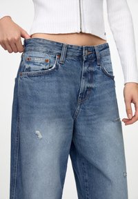 Světle modré džíny s vysokým pasem, s odřenými detaily, měděnými nýty a klasickým pětipocketovým střihem.