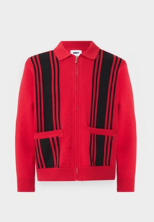 Červený pletený sveter na zips s čiernymi vertikálnymi pruhmi a dvoma vreckami vpredu, s prekladaným golierom a rebrovanými manžetami a lemom.