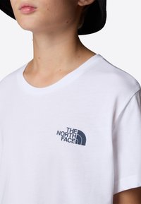 Bílá bavlněná tričko s kulatým výstřihem. Na levé části hrudi se nachází námořnickomodré logo "The North Face". Jednoduchý design.