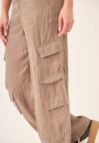 Pantalones cargo de color marrón claro, hechos de una tela suave, que cuentan con múltiples bolsillos laterales, un ajuste relajado y una textura ligeramente desgastada.