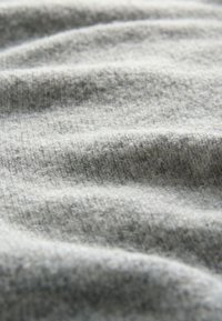 Tessuto grigio chiaro con una superficie morbida e strutturata, caratterizzato da pieghe sottili e irregolari e un aspetto leggermente sfocato.