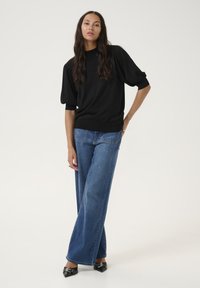Pull en maille noir à manches courtes avec un col montant, associé à un jean en denim bleu clair à jambes larges et des escarpins noirs à bouts pointus.