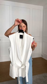 Top smanicato bianco con design avvolgente e vita legata. Realizzato in tessuto leggero, presenta un profondo scollo a V e un colletto piegato.