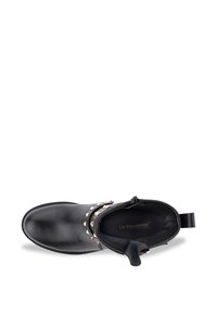 Botín negro de cuero con acabado suave, adornado con tachuelas metálicas y una tira para facilitar el calzado. El interior incluye una plantilla con la marca.