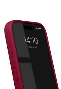 Coque de téléphone en silicone rouge avec des côtés texturés, s'adaptant à un smartphone noir affichant l'heure et la date à l'écran. Cinq barres de signal visibles.