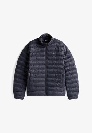 Námořnicky modrá prošívaná bunda se zapínáním na přední zip, dvěma bočními kapsami na zip a malým červeno-bílo-modrým logem na levé straně hrudi, rozložená na bílém pozadí.