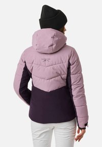 Gesteppten Jacke in Pink und Dunkelpink mit einer Kapuze, mit Chevron-Steppung und einem Logo auf dem Rücken. Rippstrick-Schwarzmütze.
