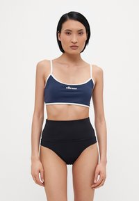 Marineblå, avkortet bikinitopp med hvit kant og logo, kombinert med høyt midje svarte bikinitruser. Glatt stoff, minimalistisk design.