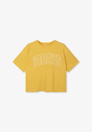 Camiseta amarilla de manga corta con cuello redondo y texto "10DAYS" en blanco contorneado, arqueado sobre el pecho, sobre un fondo blanco liso.