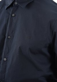 Camicia a maniche lunghe blu navy in un materiale liscio, con colletto strutturato, sei bottoni e un logo ricamato discreto sul petto.