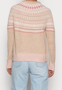 Ljusbeige tröja med ett rosa och vitt geometriskt mönster över oket. Har en rund halsringning och ribbmuddar, mjuk textur.