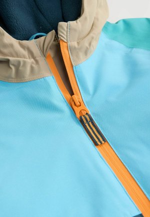 Vaaleansinisestä takista, jossa on vetoketju oranssilla vetoketjulla, beige huppu ja tumma sininen fleecevuori. Liukas, kevyt kangas.