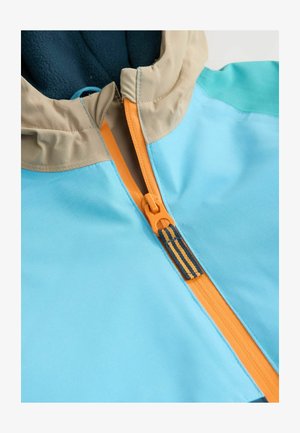 Gaiši zilā jaka ar rāvējslēdzēju, kas ir oranžā krāsā, smilškrāsas kapuces apmale un tumši zilas flīsa oderes. Gluda, viegla auduma struktūra.