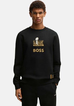 Giovane uomo che indossa una felpa nera con il logo dorato del Super Bowl LVI e la parola BOSS stampata sul davanti.