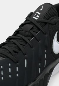 Κοντινό πλάνο μαύρου αθλητικού παπουτσιού Nike με λευκό λογότυπο Swoosh, λεπτομερείς ραφές και σφιχτά δεμένα κορδόνια πάνω από επενδεδυμένη γλώσσα με το σήμα "GT".