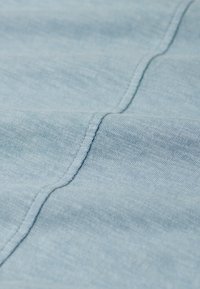 Lichtblau denimstof met een gladde textuur, voorzien van subtiele diagonale weving en een eenvoudige naad die langs de rand loopt.