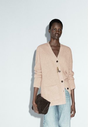 Light pink ribbed cardigan with a V-neck, buttons down the front, and a pocket. Paired with pale blue denim and a dark brown clutch.