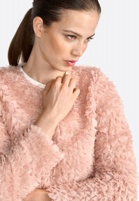 Maglione rosa strutturato con un design sfocato e stratificato. Presenta un colletto rotondo e maniche lunghe, evidenziando un aspetto morbido e delicato.