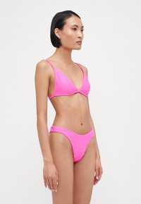 Costum de baie ribbed de culoare roz aprins, cu un top în formă de triunghi și o parte de jos cu talie înaltă. Curelele subțiri și textura netedă îmbunătățesc designul.