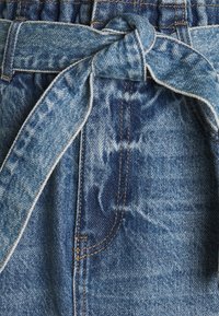 Jeanshorts med knytband i midjan, med ljusblå och mörkblå blekta mönster, synlig sömnad och texturerad tygdetalj.