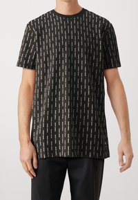 Svart kortärmad t-shirt med ett upprepande vitt logomönster, rund halsringning och avslappnad passform. Tillverkad av mjukt tyg.