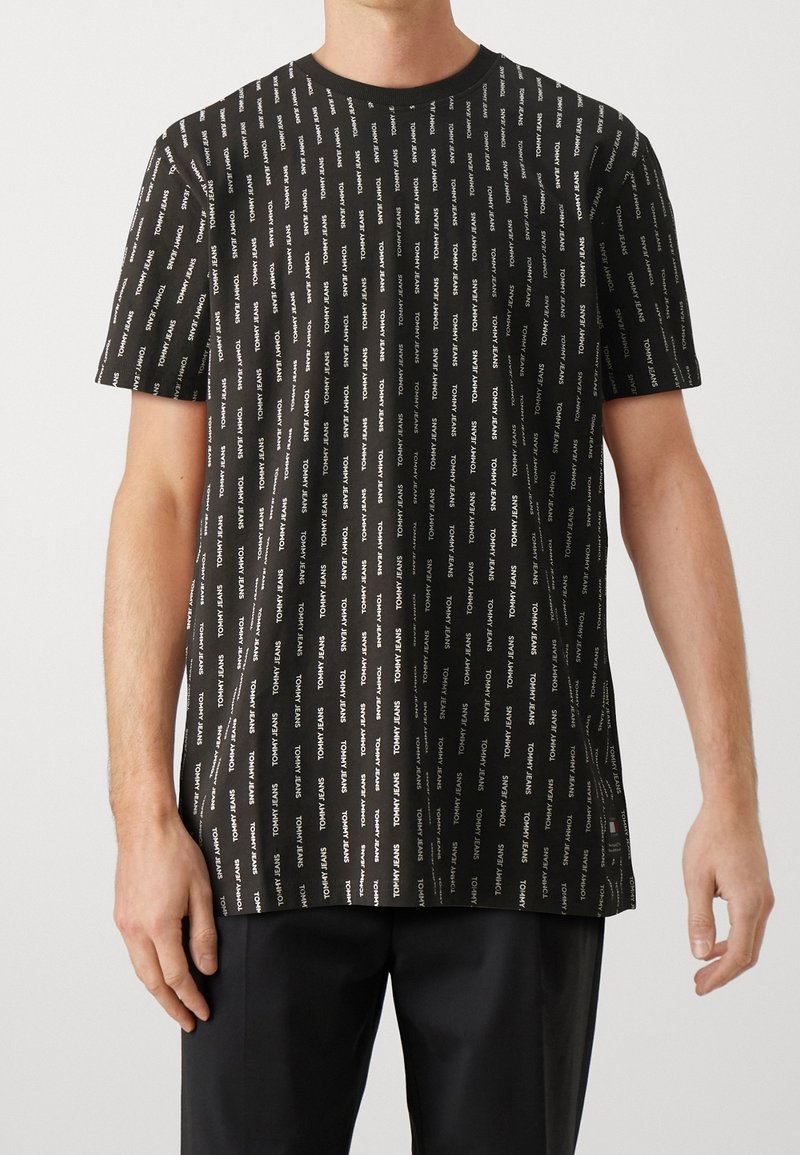 Svart kortärmad t-shirt med ett upprepande vitt logomönster, rund halsringning och avslappnad passform. Tillverkad av mjukt tyg.