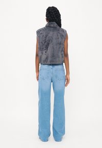Grijze faux fur mouwloze vest in combinatie met lichtblauwe wijde jeans, met achterzakken en een relaxte pasvorm. Minimalistisch ontwerp.