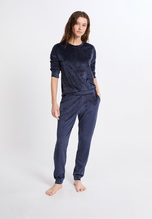 Conjunto de loungewear de terciopelo azul marino que incluye una camiseta de manga larga con patrones de corazones y pantalones ajustados a juego con bolsillos laterales.