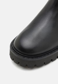 Stivale alla caviglia in pelle nera con punta arrotondata, finitura testurizzata e suola in gomma nera robusta con profonde scanalature per una buona trazione.