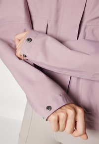 Light purple jacket with a smooth texture, featuring a buttoned cuff, and contrasting stitching. The fabric appears water-resistant.