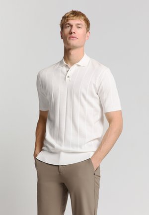 Witte polo shirt met korte mouwen, voorzien van een gestructureerd breipatroon, een drieknoopsluiting en ribgebreide rand, gecombineerd met lichtbruine broeken.