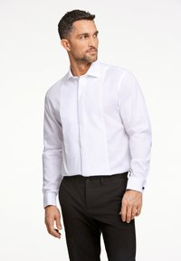 Camicia bianca con un pannello frontale testurizzato, colletto classico e polsini a un bottone. Abbinata a pantaloni neri slim-fit.