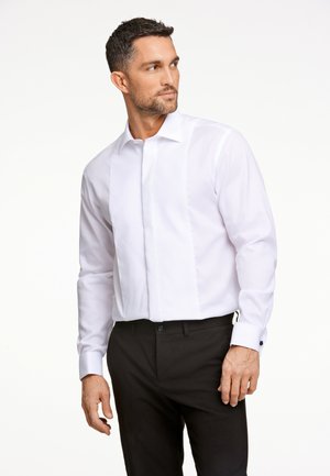 Witte bloes met een gestructureerd voorpaneel, klassieke kraag en manchetten met één knoop. Gecombineerd met slim-fit zwarte broek.