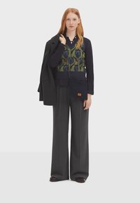 Pull en tricot avec un motif floral dans des teintes de vert et de bleu, associé à un haut uni marine et un pantalon large à fines rayures grises. Blazer noir drapé.
