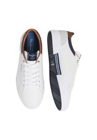 White sneakers with a smooth leather upper, contrasting navy and tan accents, lace-up closure, and textured black rubber outsole.
