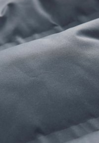 Textūruotas pilkas audinys su lygiu paviršiumi, turintis subtilių raukšlių ir švelnų išvaizdą. Matomų raštų ar puošmenų nėra.