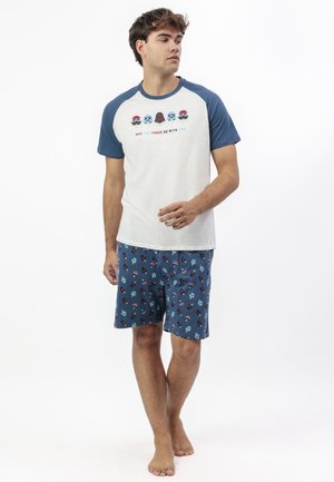 Hombre con camiseta raglán azul y blanca con cascos de Star Wars y texto, combinado con pantalones cortos azules con estampado de cascos de Star Wars.