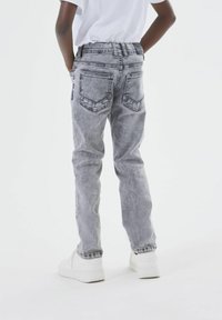 Vaqueros de denim gris con un corte relajado, que cuentan con bolsillos traseros y un deslavado sutil. Combinados con zapatillas blancas, vistos desde la parte de atrás.