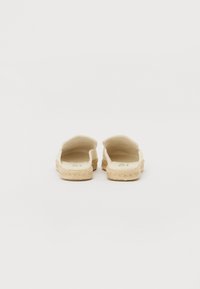 Kreminės espadrilės su atvira nugarėle, audinio viršus ir pintas džutas padais. Pasižymi lygiu paviršiumi ir minimalistiniu dizainu.